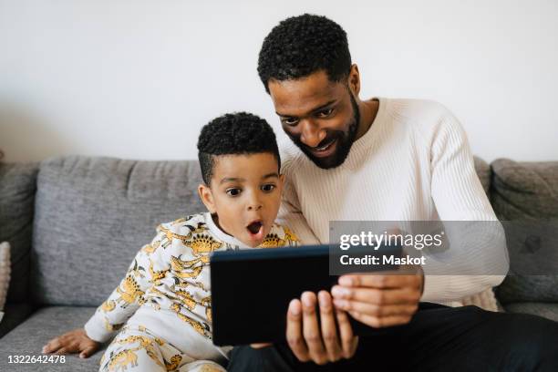 father and son watching video on digital tablet at home - using tablet young stock-fotos und bilder