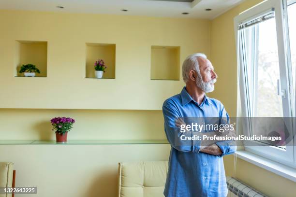 portrait of a thoughtful senior man standing near the window. - good; times bad times stock pictures, royalty-free photos & images