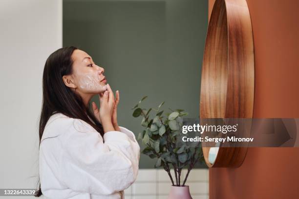 young asian woman applying moisture cream at her face - etnia coreana fotografías e imágenes de stock