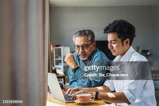 Asian senior father and his adult son using laptop computer while sitting at home Asian senior father and his adult son using laptop computer while sitting at home