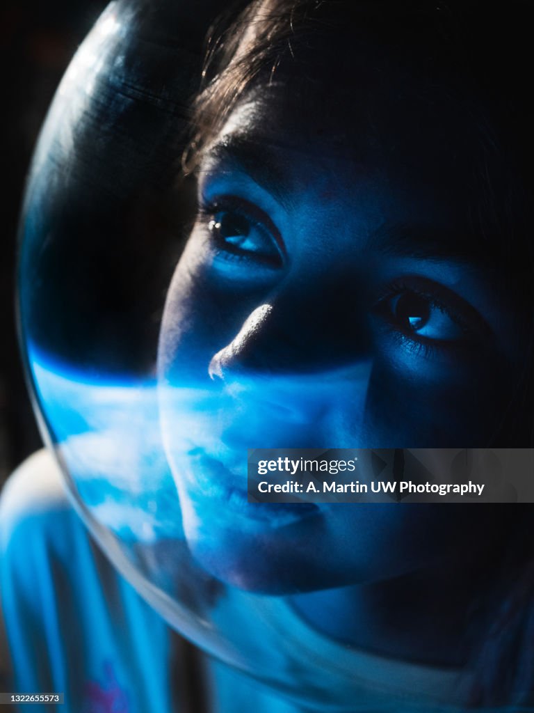 Young astronaut wearing a space helmet and looking to the earth through the space shuttle window. Space journey concept.