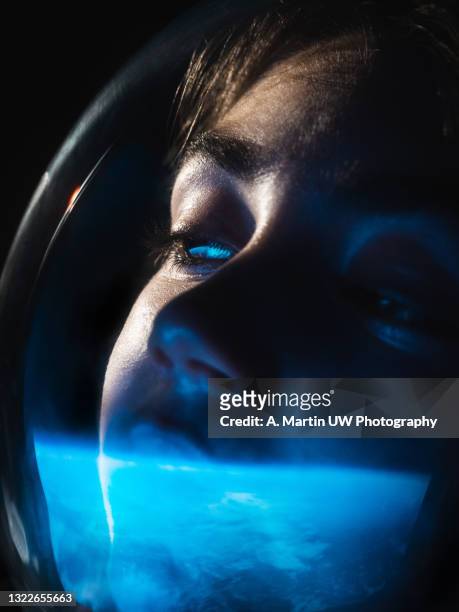 young astronaut wearing a space helmet and looking to the earth through the space shuttle window. space journey concept. - girl rising stock-fotos und bilder