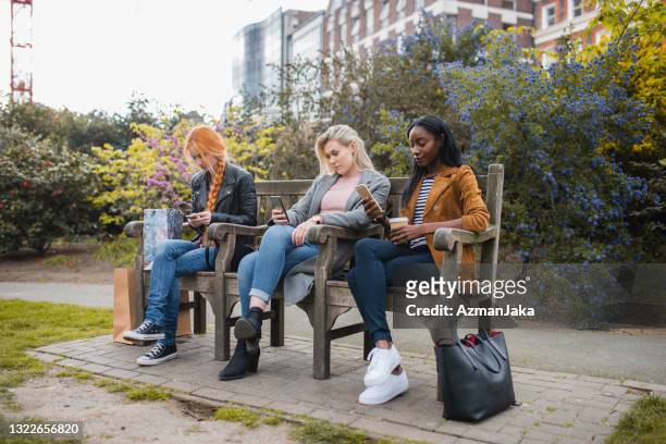group of women using their mobile phones while sitting on park bench in london, england - 2017 common good forum stock pictures, royalty-free photos & images