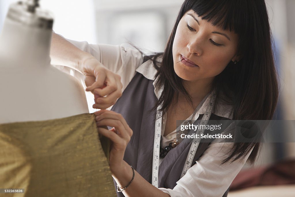 Young female designer pinning fabric to mannequin