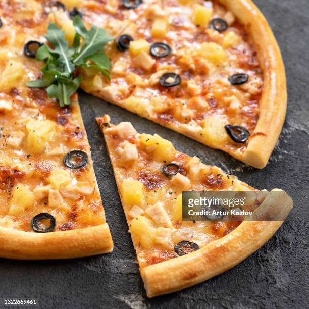 pizza with pineapple and olives. close-up shot of sliced pizza and large slice of it on black background. vegan or vegetarian meal. italian junk food delivery concept. soft focus - ananas photos et images de collection