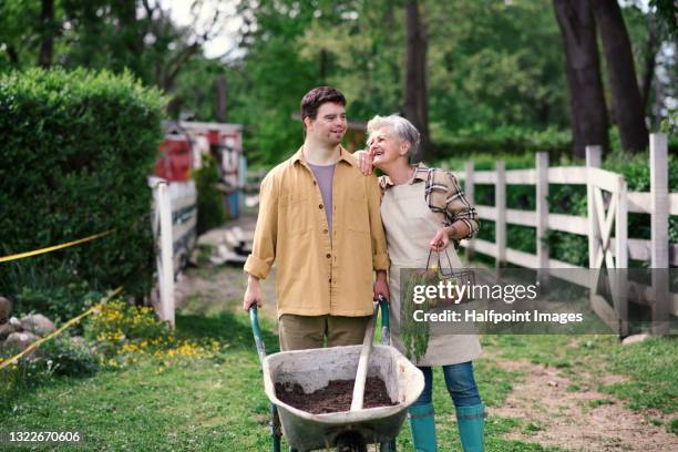 senior woman and down-syndrome man walking on farm, community farming. - down's syndrome fotografías e imágenes de stock