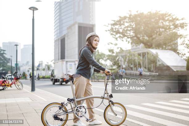 indonesian woman walking on a zebra crossing with her bike - geplooid stockfoto's en -beelden