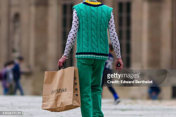 Passerby wears a pearls necklace, a green wool woven sleeveless pullover, a white with black moon pattern long sleeves t-shirt from Marine Serre,...
