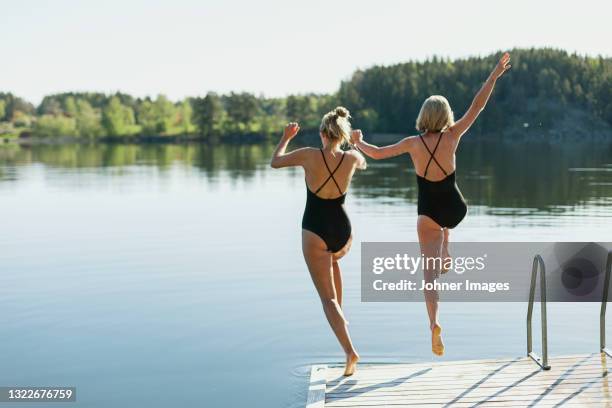 women jumping into lake from deck - lake stock-fotos und bilder