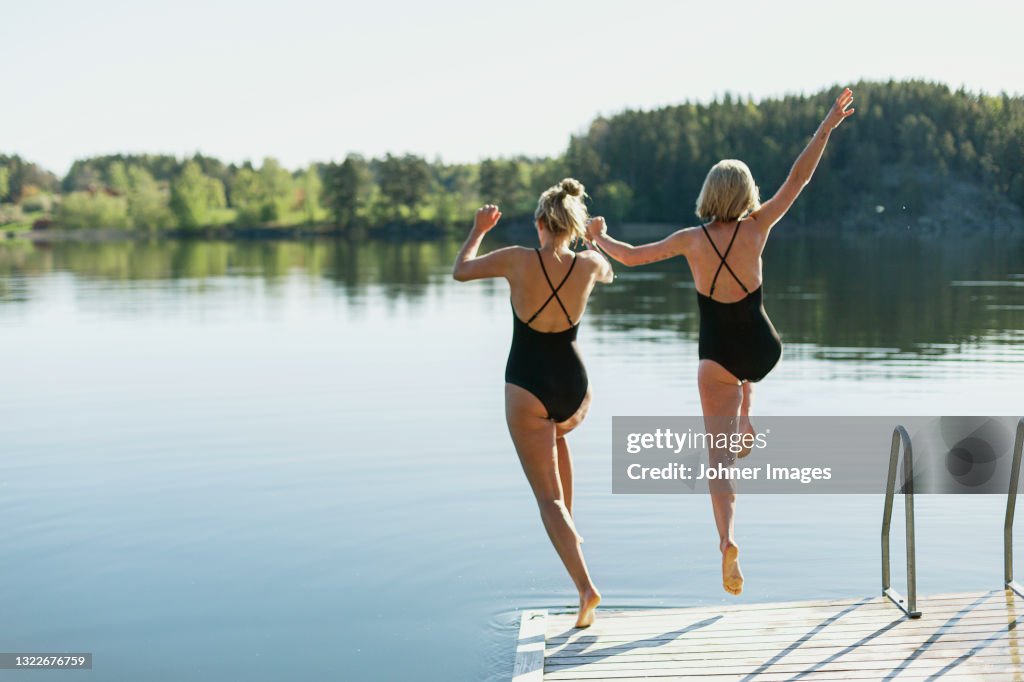 Women jumping into lake from deck