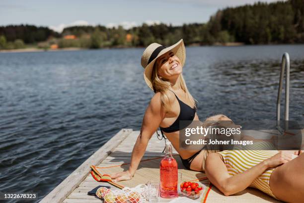 smiling women in swimsuits relaxing at lake - besparen stockfoto's en -beelden