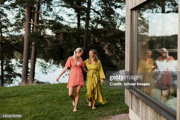 smiling female friends walking in backyard - women in see through dresses stock-fotos und bilder