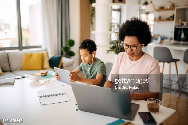 mother is having business meeting while her son is on digital tablet next to her - mother and son using tablet and laptop stock pictures, royalty-free photos & images