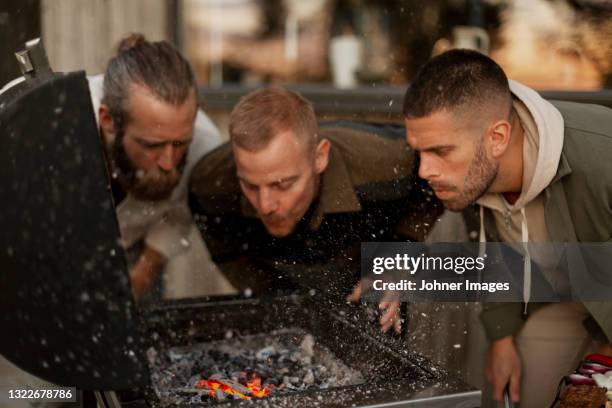 male friends blowing on barbecue - friends male stock-fotos und bilder