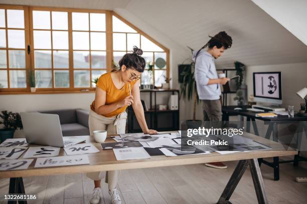 woman busy working at new home office with her coworker behind her - grafisch ontwerpbureau stockfoto's en -beelden