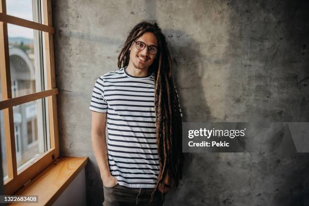 lächelnder mann mit dreadlocks posiert für einen schuss vor betonwand - dreadlocks stock-fotos und bilder