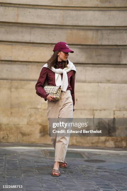 Therese Hellström wears a burgundy logo Celine cap, a brown shirt with pearls buttons and lace flower detail on the sleeves, a white wool pullover, a...