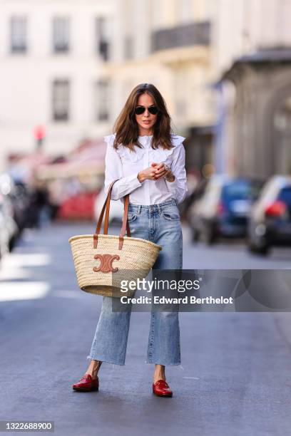 Therese Hellström wears black Ray Ban sunglasses, a white shirt with lace puffy collar, blue faded denim jeans pants, a beige wicker and brown shiny...