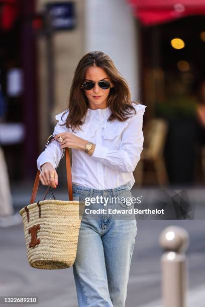 Therese Hellström wears black Ray Ban sunglasses, a white shirt with lace puffy collar, blue faded denim jeans pants, a beige wicker and brown shiny...