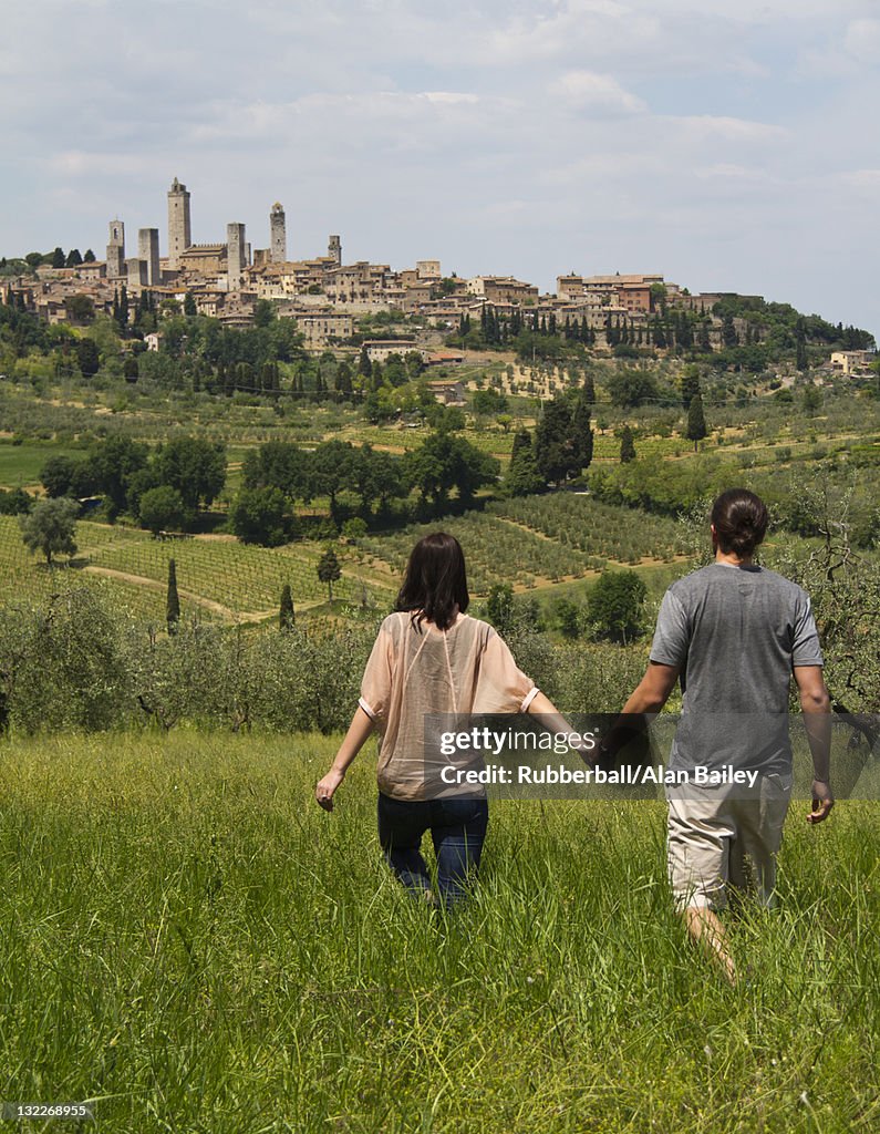 Italy, Tuscany, San Gimignano, Rear view of young couple walking on meadow