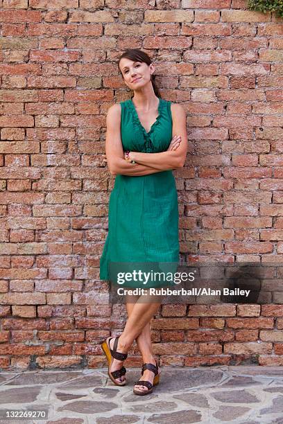 italy, burano, portrait of mature woman leaning against brick wall - green dress 個照片及圖片檔