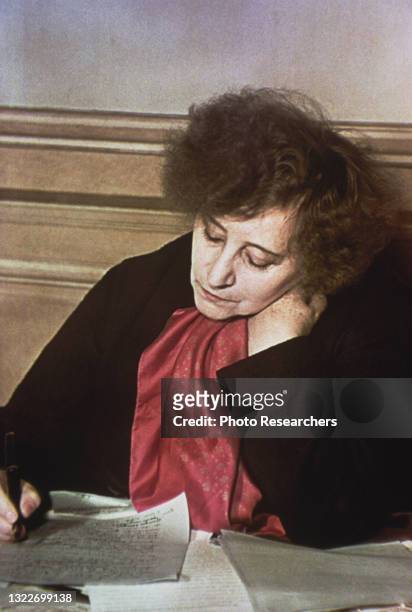 View of French author Colette as she writes with pen at a table, Paris, France, 1939.