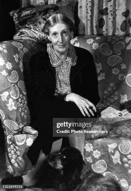 Portrait of English author Virginia Woolf as she sits cross-legged on a couch, with her Cocker Spaniel, Pinka, at her feet, London, England, 1939.