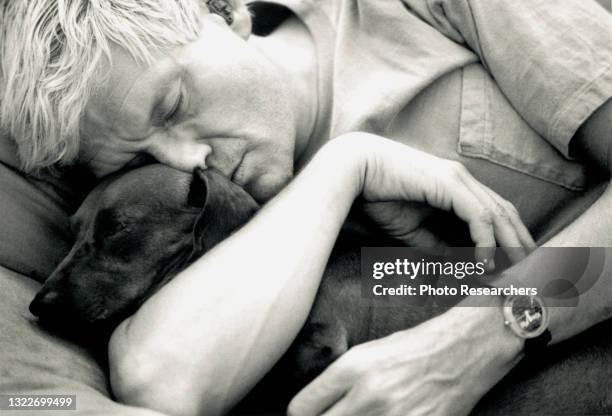 View of British Pop artist David Hockney as he holds one of his pet dachshunds, 1993.