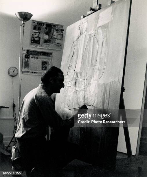 View of American Pop artist and musician Larry Rivers as he paints on a canvas in his Chelsea Hotel studio, New York, New York, 1964.