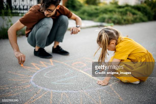little girl and dad draw with chalk on the concrete - family chalk drawing stock pictures, royalty-free photos & images