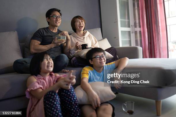 asian chinese family sitting on sofa watching television at home together. - asian watching movie stock pictures, royalty-free photos & images