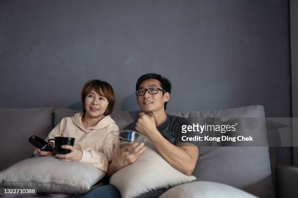 asian chinese couple sitting on sofa watching tv movies at home. - film screening room stock pictures, royalty-free photos & images