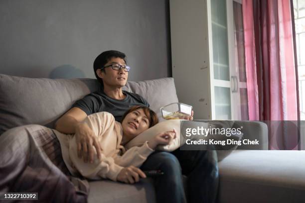 aziatische chinese paarzitting op bank die tv-films thuis bekijkt. - film and television screening stockfoto's en -beelden