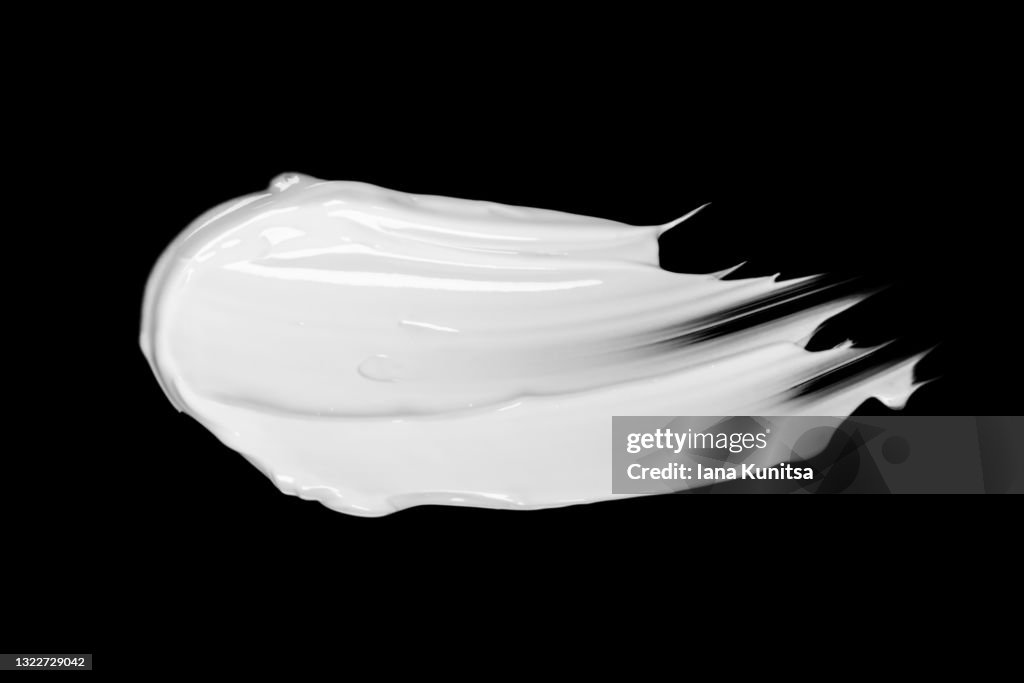 White face cream smear on black background isolated. Cosmetic products for makeup and skin care.
