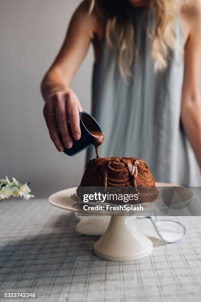 för chokladälskare: hand av en anonym kvinna som häller lite chokladglasyr över en utsökt bundt-tårta - glaserad mat bildbanksfoton och bilder