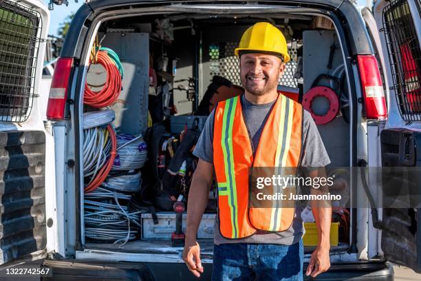 lächelnder hispanischer bauarbeiter mit arbeitshelm, der in die kamera schaut - lieferwagen stock-fotos und bilder
