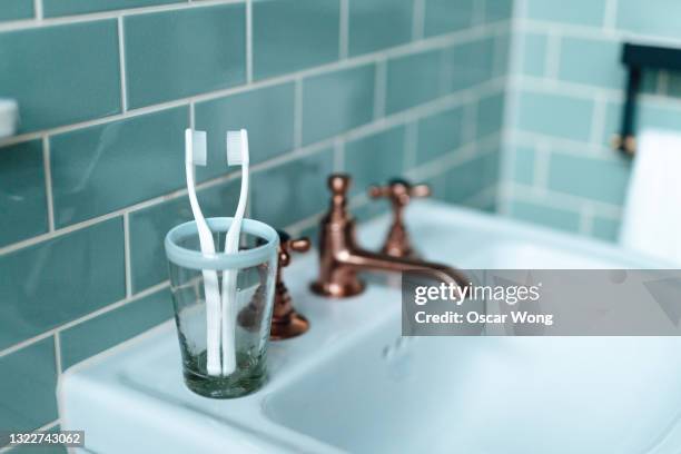 two toothbrushes in cup sitting on bathroom sink - bathroom clean closeup stock-fotos und bilder