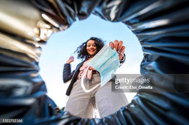 mujer que arroja máscara quirúrgica protectora usada al cubo de basura desde el interior - throwing fotografías e imágenes de stock