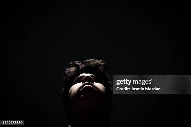 young guy in shadows looking up - dark background light stock-fotos und bilder