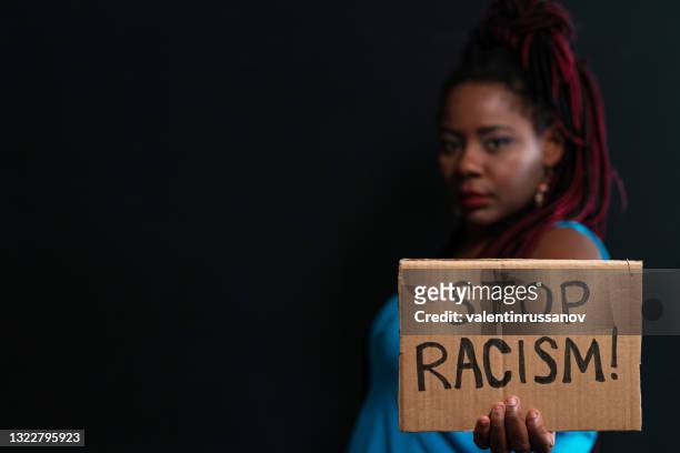 african american women standing on a black background and looking at the camera. she is showing message that says stop racism - black civil rights stock pictures, royalty-free photos & images