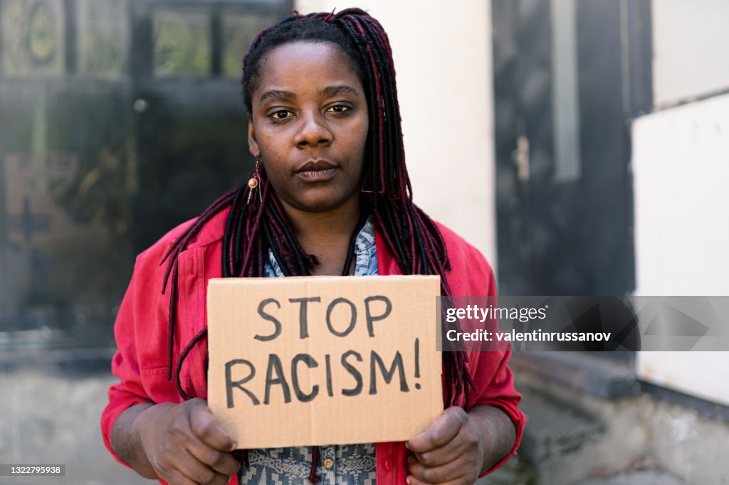African american women standing in front of an iron door and showing message that says Stop Racism
