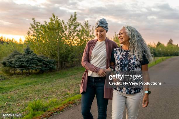 ethnic woman with cancer and her affectionate mother walking arm in arm at sunset - rural scene stock pictures, royalty-free photos & images