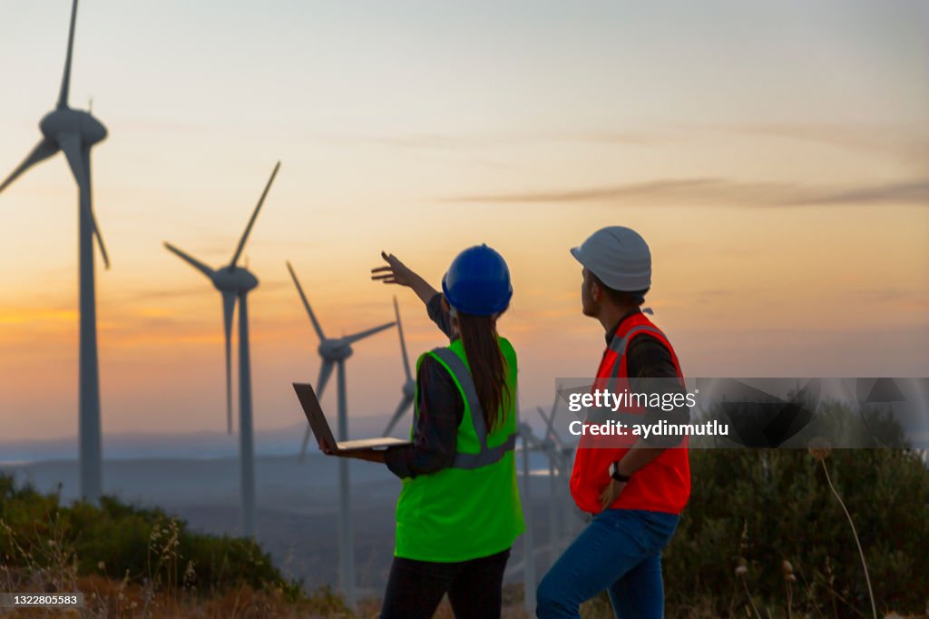 Young maintenance engineer team working in wind turbine farm at sunset