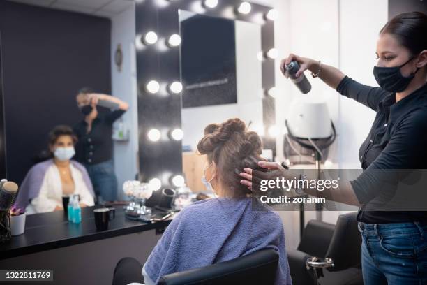 friseur trägt schützende gesichtsmaske auf, sprühen haarspray kunden haare - hairspray stock-fotos und bilder