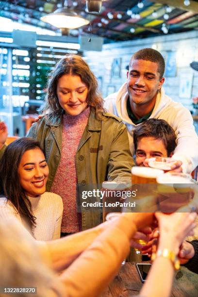 group of happy friends having fun in a pub drinking ice cold beers - beer cheers stock pictures, royalty-free photos & images