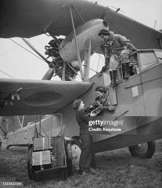Radio technician of the Women's Royal Naval Service collects a radio transmitter from the navigator as the Air Transport Auxiliary ferry pilot climbs...