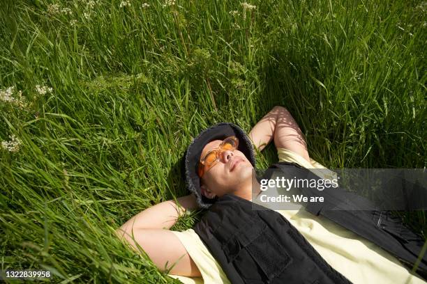 man lying back in long grass enjoying the sunshine - tomar sol fotografías e imágenes de stock