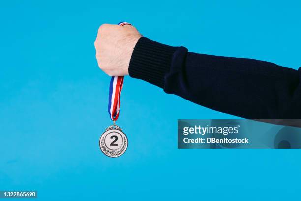 detail of an elderly athlete's arm holding a first place gold medal, on blue background. - ranking stockfoto's en -beelden