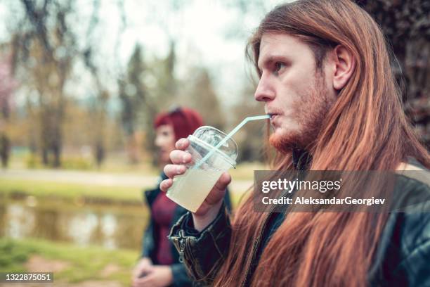 metalhead macho y mujer gótica bebiendo jugo en el parque - heavy fotografías e imágenes de stock