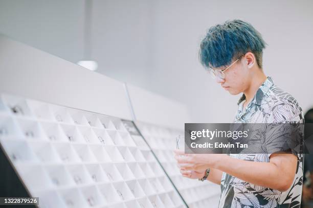 asiatisk kinesisk tonårspojke med färgat hår som försöker på glasögon framför spegeln på optikerbutik - teenager boy shopping bildbanksfoton och bilder